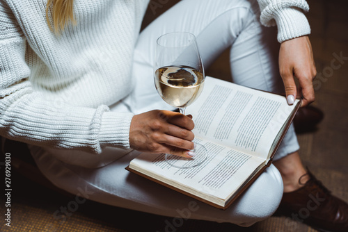 cropped view of woman holding wine glass and book in library