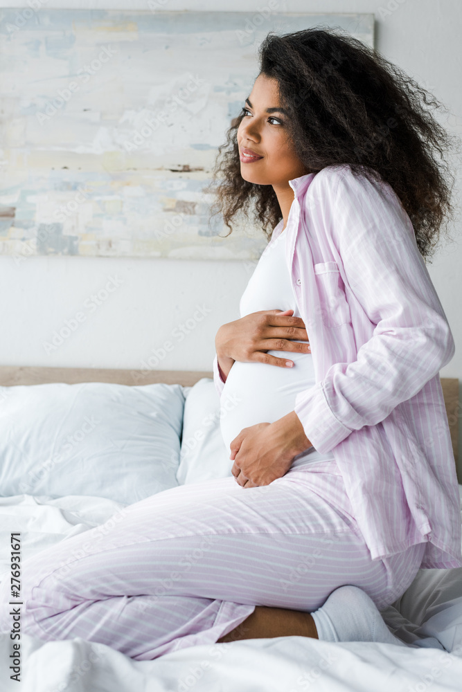 positive young pregnant african american woman sitting on bed