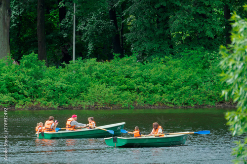 PEOPLE IN RESCUE VESTASES WALK ON A BOAT WITH OARS IN THE ENVIRONMENT OF GREEN TREES