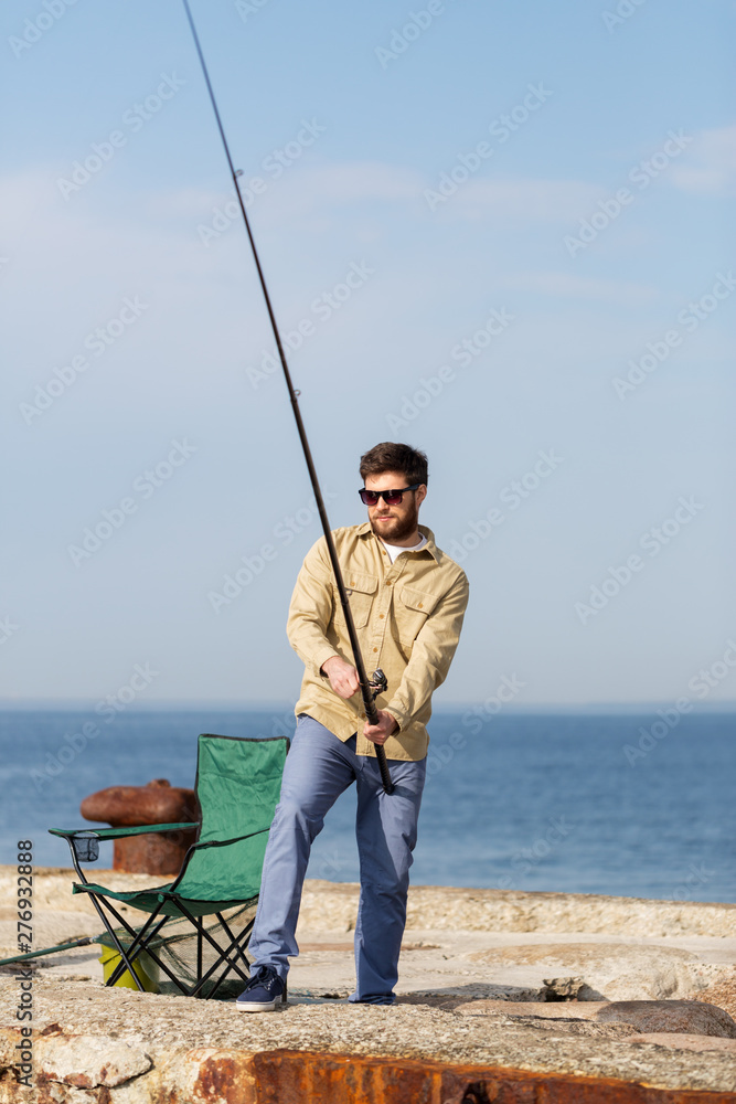 leisure and people concept - bearded fisherman with fishing rod on sea pier