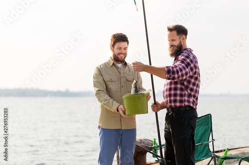 leisure and people concept - happy male friends with fish and fishing rods on pier at sea