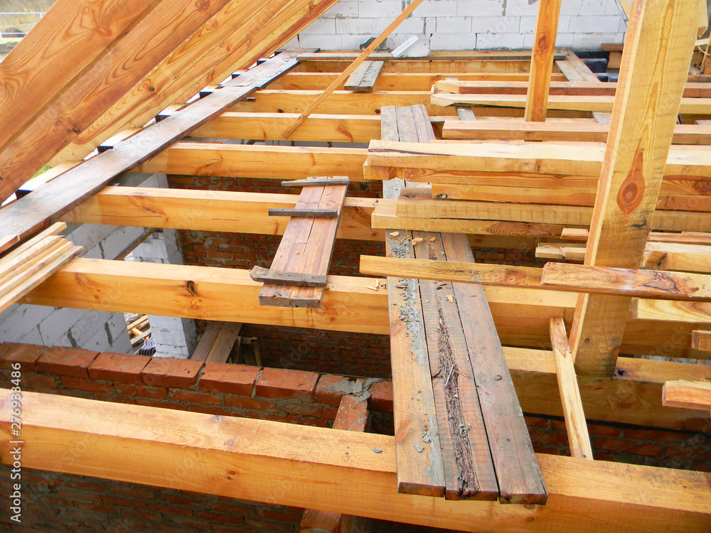 Unfinished attic house roofing construction trusses, wooden beams, eaves, timber. House roof wooden frame construction. Unfinished attic house roofing construction trusses, wooden beams, eaves, timber. House roof wooden frame construction.
