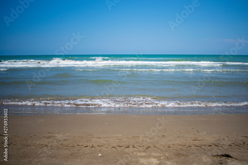 Mar azul turqueza en calma, con olas pequeñas y cielo azul despejado, con arena dorada