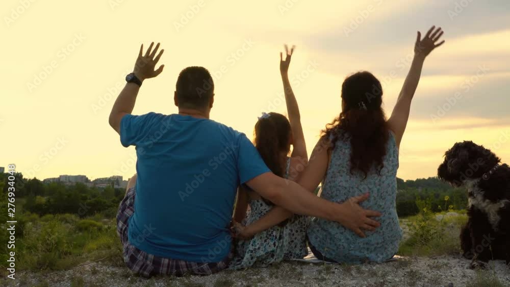 Happy family: dad, mom, little daughter and dog sitting on top of the hill at sunset summer day. They smile and wave to the setting sun. The concept of family happiness. Close-up. Rear view. 4K Happy family: dad, mom, little daughter and dog sitting on top of the hill at sunset summer day. They smile and wave to the setting sun. The concept of family happiness. Close-up. Rear view. 4K