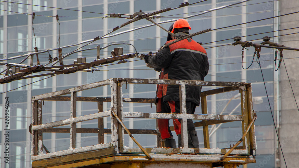 Workers on the tower repair the contact mains network for trolley buses
