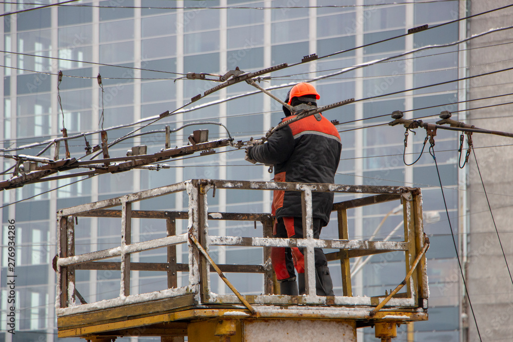 Workers on the tower repair the contact mains network for trolley buses