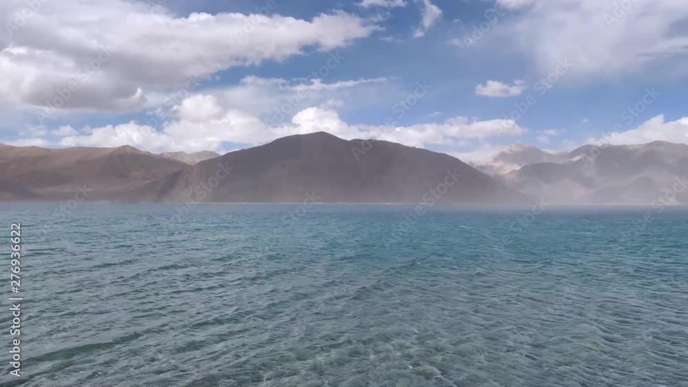Dust storm over the Crystal clear water of the Pangong Tso lake (world's highest saltwater lake at 14,000ft) with dry mountains behind it. (4k, 60fps, High definition, 1080p). Dust storm over the Crystal clear water of the Pangong Tso lake (world's highest saltwater lake at 14,000ft) with dry mountains behind it. (4k, 60fps, High definition, 1080p).