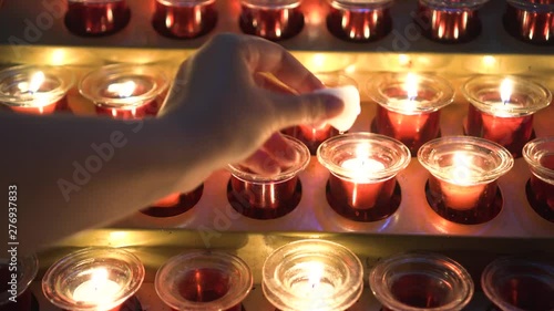 POV Girl lights a candle and puts in red glass candle holder Many lit candles shining in church