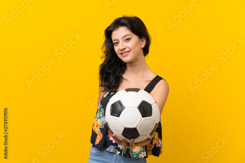 Young woman over isolated yellow background holding a soccer ball © luismolinero
