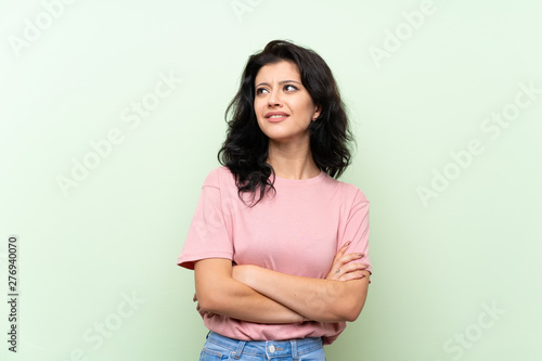 Young woman over isolated green background looking up while smiling