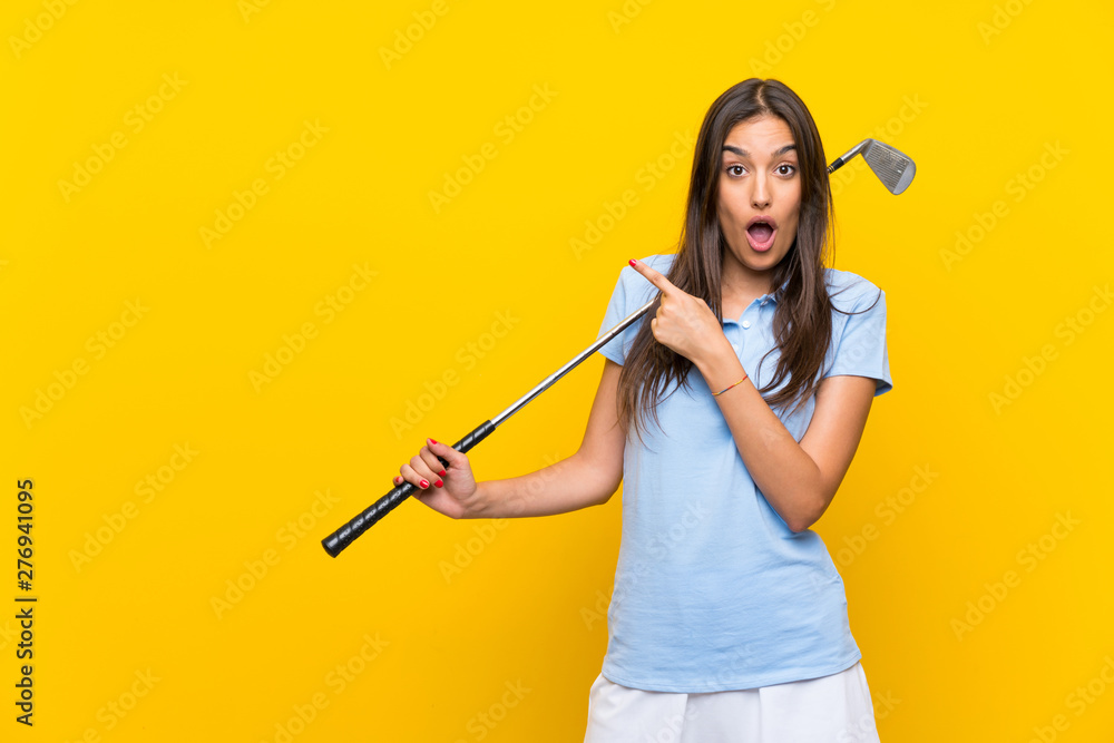 Young golfer woman over isolated yellow wall surprised and pointing side Young golfer woman over isolated yellow wall surprised and pointing side