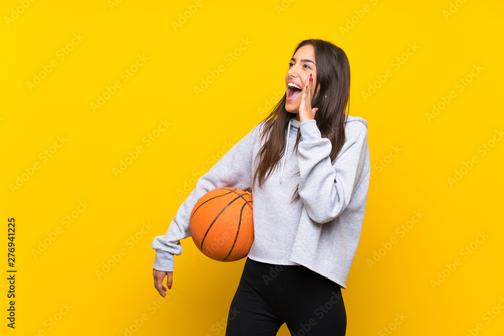 Young woman playing basketball over isolated yellow background shouting with mouth wide open Young woman playing basketball over isolated yellow background shouting with mouth wide open