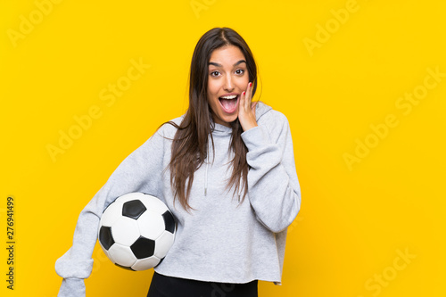 Young football player woman over isolated yellow background with surprise and shocked facial expression © luismolinero