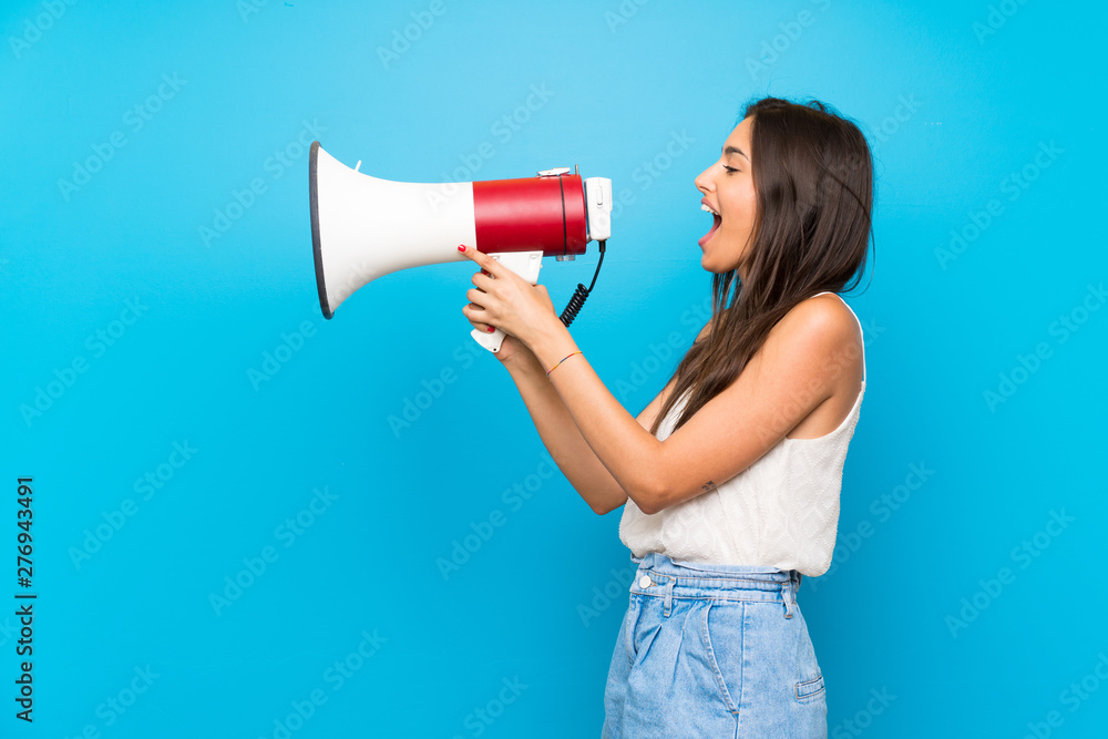 Young woman over isolated blue background shouting through a megaphone Young woman over isolated blue background shouting through a megaphone