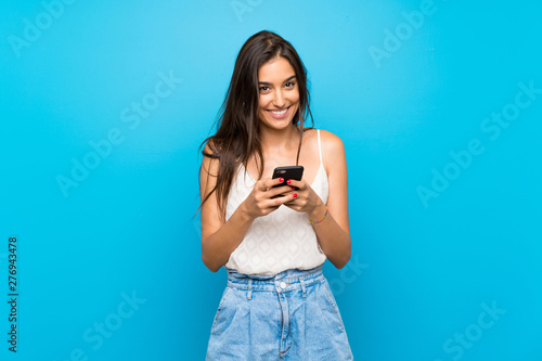 Young woman over isolated blue background sending a message with the mobile