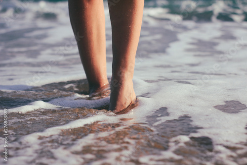 Female legs in the water. The girl goes along the coastline. Sunset light and sea foam. © exienator