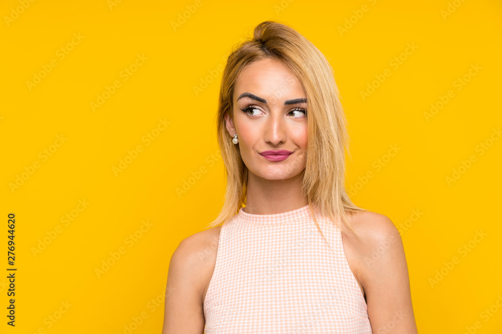 Young blonde woman over isolated yellow wall standing and looking to the side Young blonde woman over isolated yellow wall standing and looking to the side