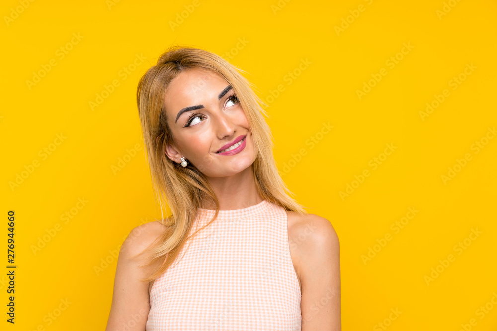 Young blonde woman over isolated yellow wall laughing and looking up Young blonde woman over isolated yellow wall laughing and looking up