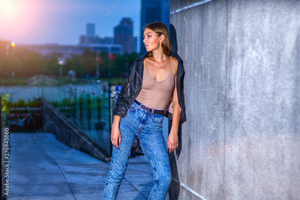 Beautiful girl in jeans and leather jacket is posing fashionable near