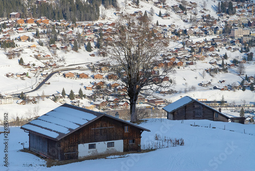Old wooden barn in the winter mountains and Grindelwald village in the valley in Bernese Alps In Switzerland.