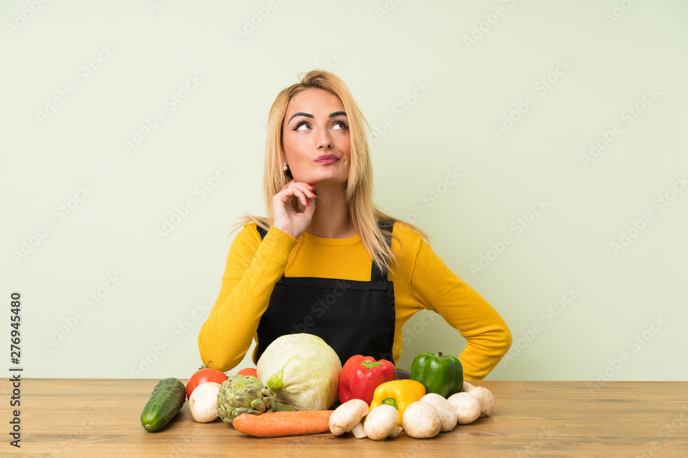 Fototapeta premium Young blonde woman with lots of vegetables thinking an idea