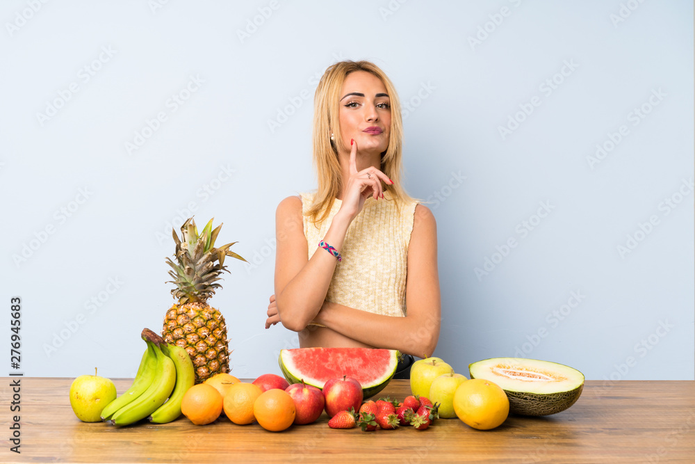 Young blonde woman with lots of fruits thinking an idea