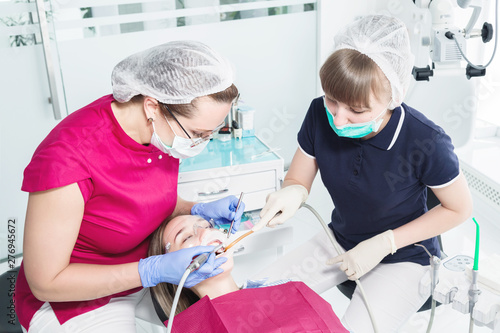 Female dentist and nurse doing professional care and tooth brushing of a young patient in a dental office