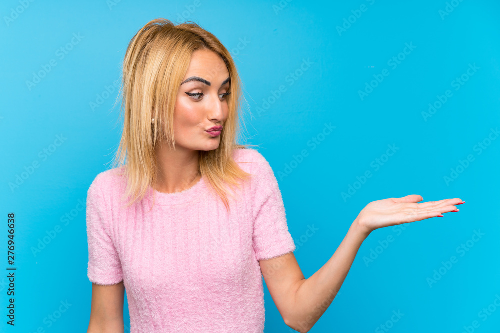 Fototapeta premium Young blonde woman over blue background holding copyspace imaginary on the palm