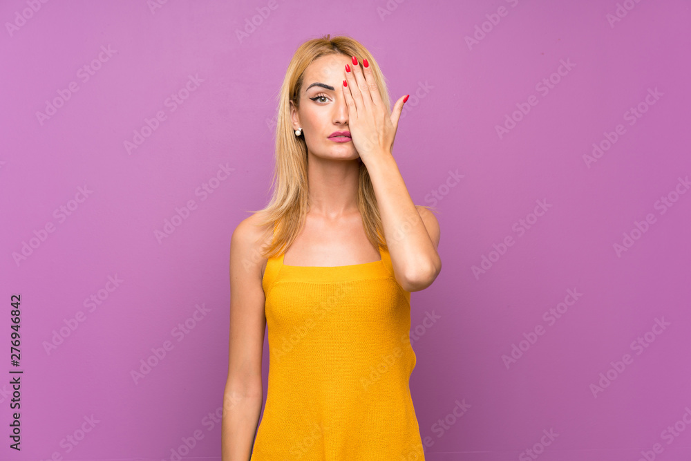 Young blonde woman over purple background covering a eye by hand Young blonde woman over purple background covering a eye by hand