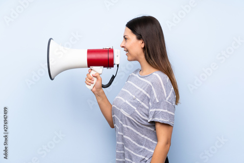 Young brunette woman over isolated blue background shouting through a megaphone