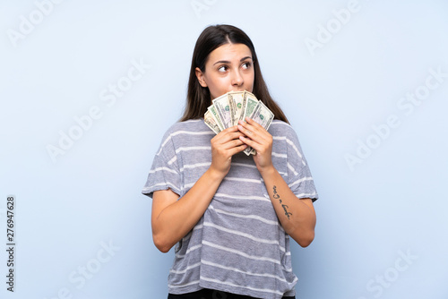 Young brunette woman over isolated blue background taking a lot of money