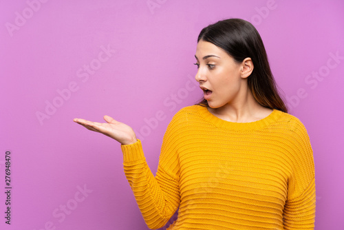 Young woman over isolated purple background holding copyspace imaginary on the palm