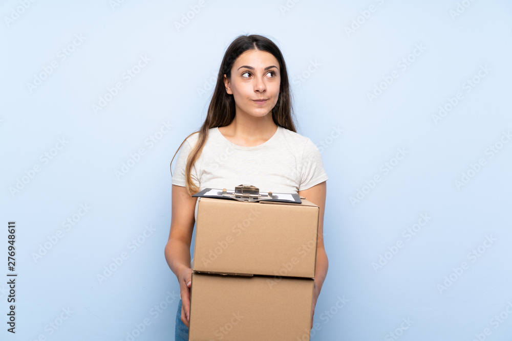 Young delivery woman over blue brick wall looking up while smiling Young delivery woman over blue brick wall looking up while smiling