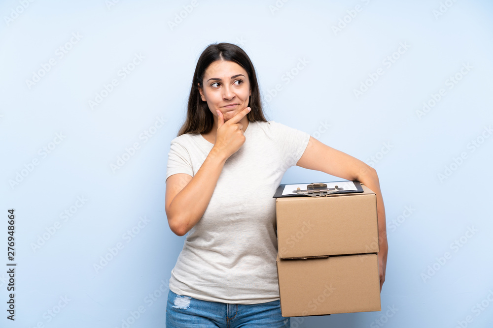 Young delivery woman over blue brick wall thinking an idea Young delivery woman over blue brick wall thinking an idea