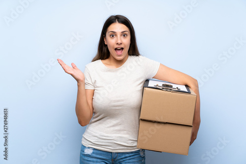 Young delivery woman over blue brick wall with shocked facial expression