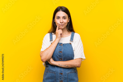 Young woman in dungarees over isolated yellow background Looking front