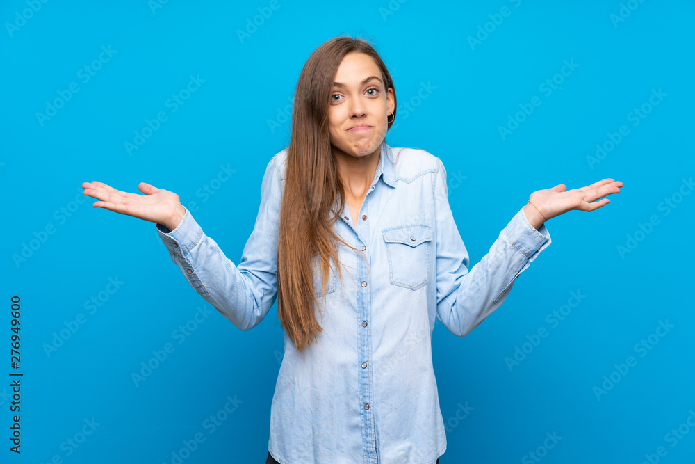 Young woman over isolated blue background having doubts while raising hands Young woman over isolated blue background having doubts while raising hands