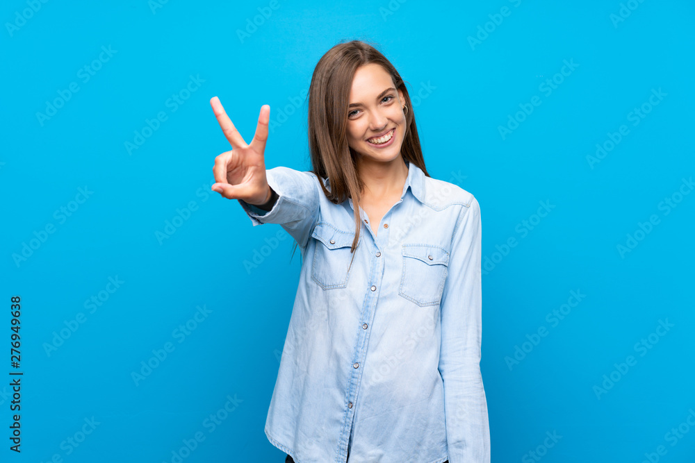 Young woman over isolated blue background smiling and showing victory sign Young woman over isolated blue background smiling and showing victory sign