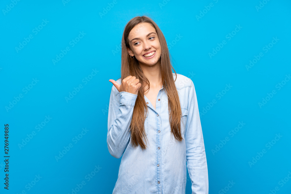 Young woman over isolated blue background pointing to the side to present a product Young woman over isolated blue background pointing to the side to present a product