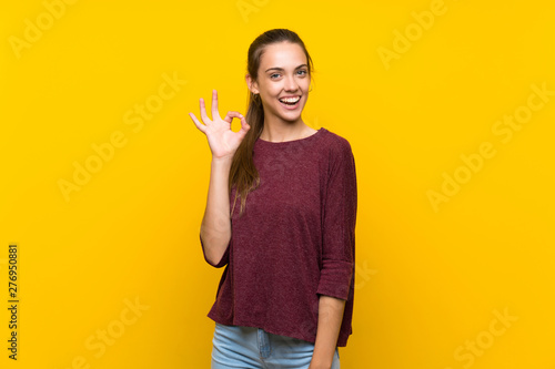 Young woman over isolated yellow background showing ok sign with fingers