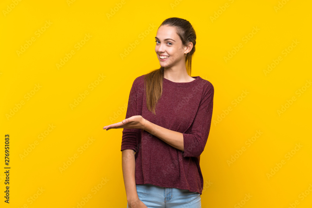 Young woman over isolated yellow background presenting an idea while looking smiling towards Young woman over isolated yellow background presenting an idea while looking smiling towards