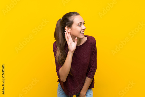 Young woman over isolated yellow background listening to something by putting hand on the ear © luismolinero