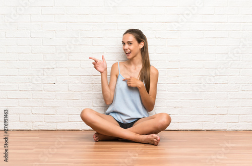 Young woman sitting on the floor pointing finger to the side