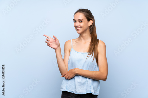 Young woman over isolated blue background pointing finger to the side