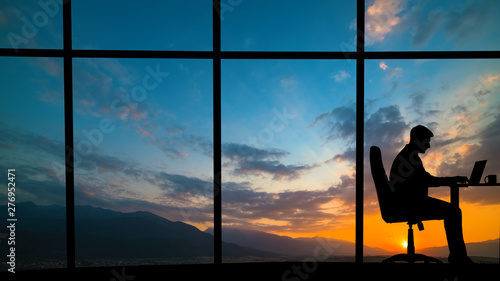 The man working at the table near a window on a mountain sunset background © realstock1