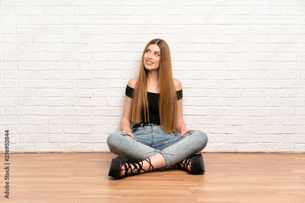 Young woman sitting on the floor laughing and looking up Young woman sitting on the floor laughing and looking up
