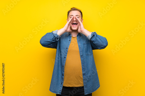 Blonde man over isolated yellow wall shouting and announcing something