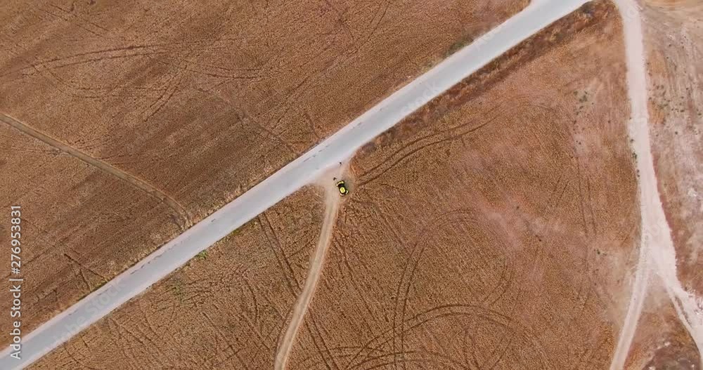 Top down view of the tourist car standing on the roadside in the middle of large agricultural wheat field. Drone view of the harvesting farmland and car on summer sunny day. Top down view of the tourist car standing on the roadside in the middle of large agricultural wheat field. Drone view of the harvesting farmland and car on summer sunny day.
