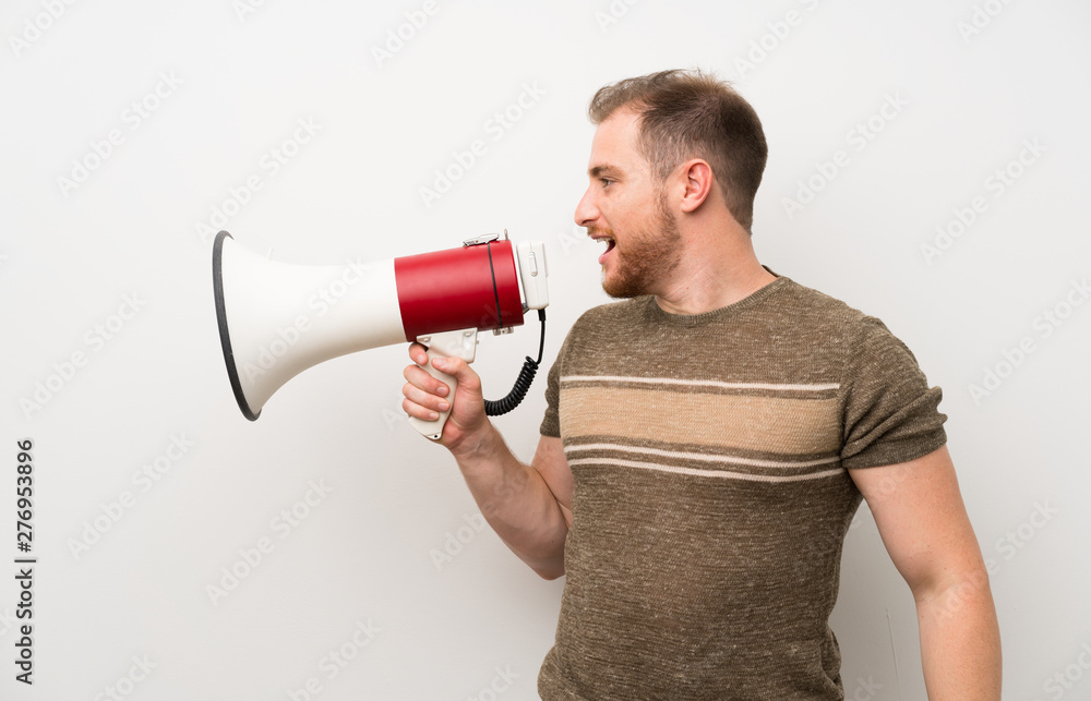 Handsome man over isolated white wall shouting through a megaphone Handsome man over isolated white wall shouting through a megaphone