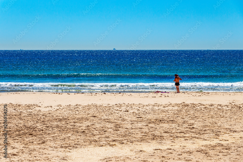 A couple at the empty Playa de los Lances or Los Lances Beach, silhouette of a fishing boat in the distance in Tarifa, Spain